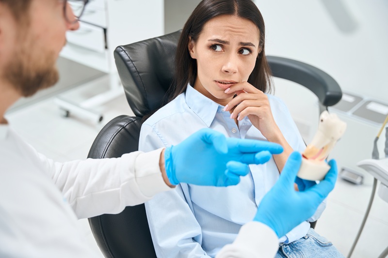 Scared woman patient attentively listening to dental technician who explaining way of her tooth extraction treatment on plastic tooth model, private clinic