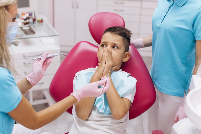 The boy is scared and closes his mouth with his hands on a visit to the dentist at the dental clinic