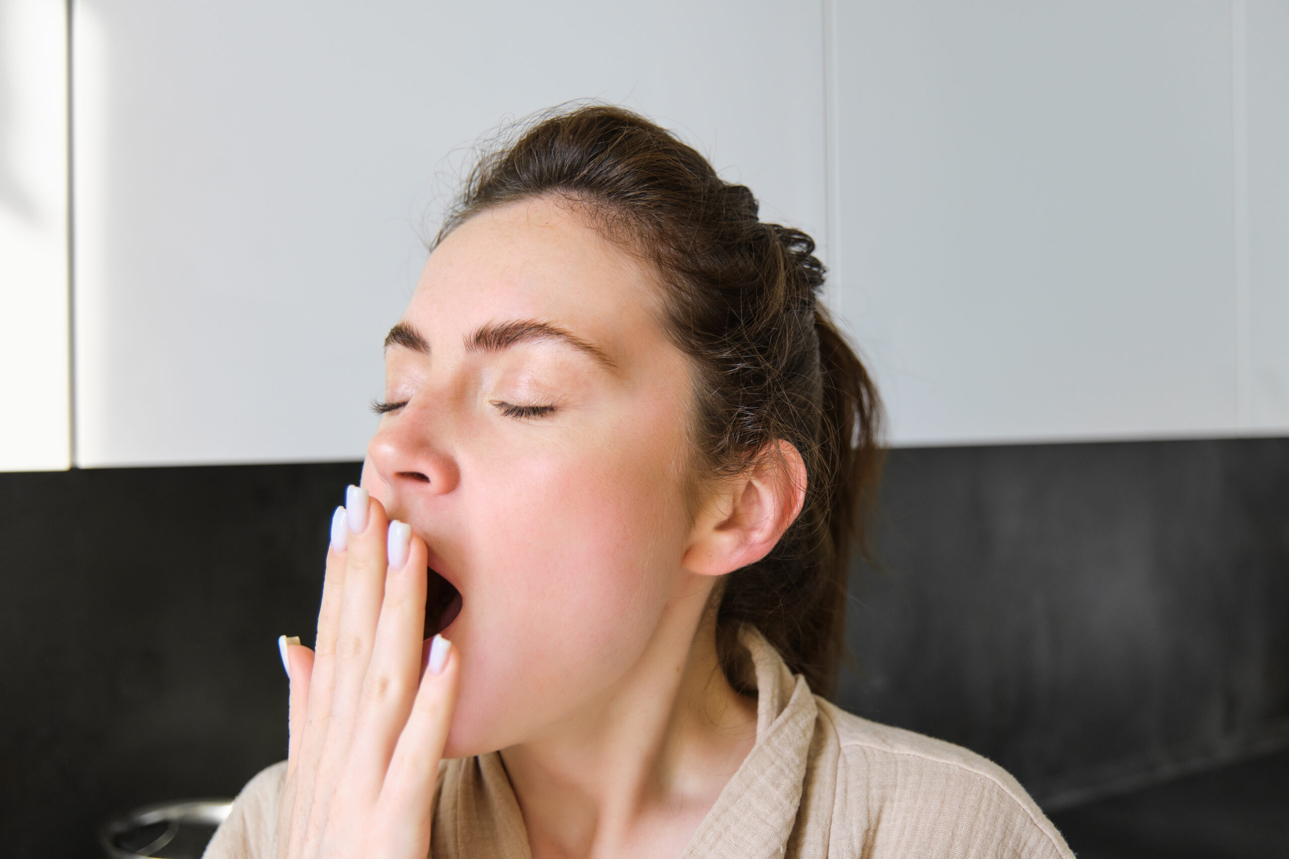 Woman yawning and covering her mouth with her hand, showing morning dryness, one of the common bad breath causes