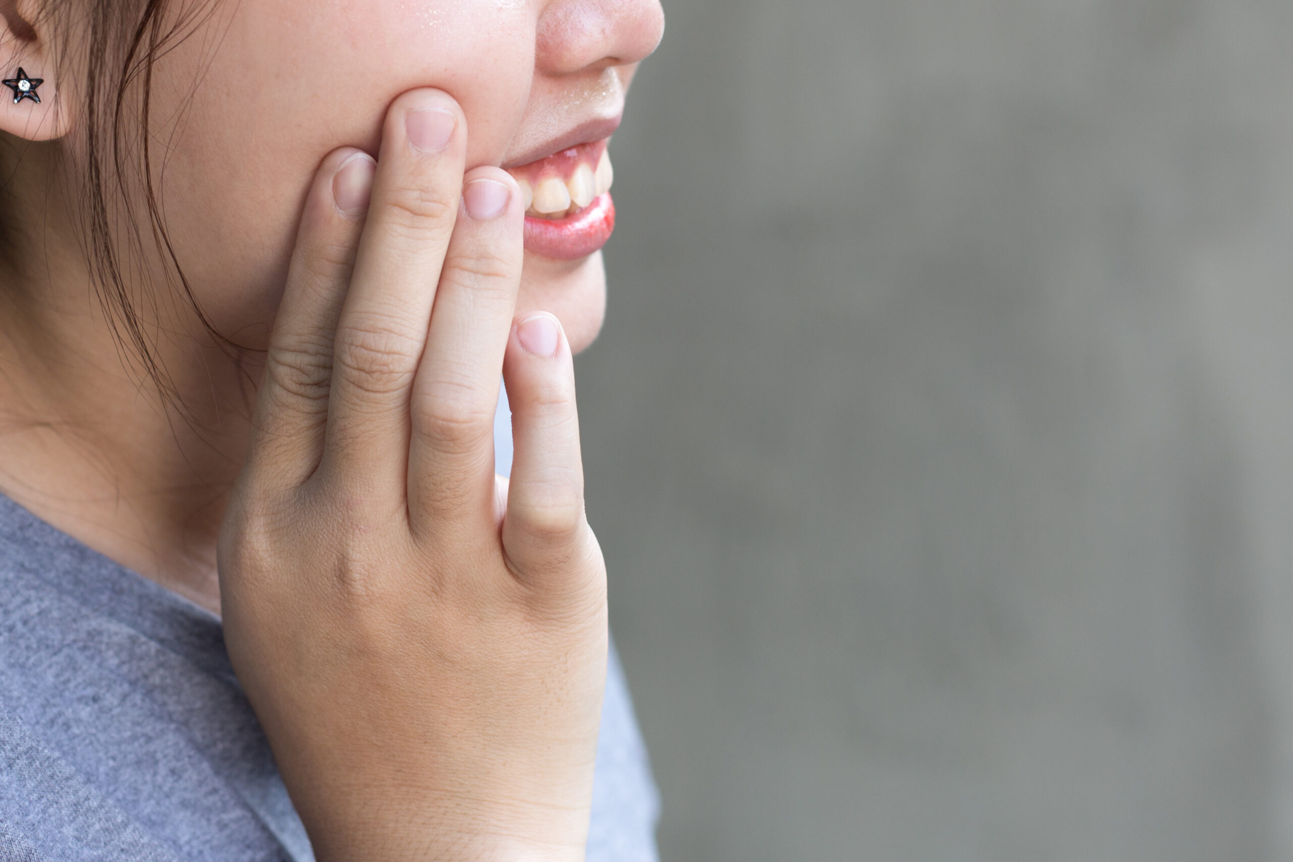 Woman pressing her fingers to her cheek, showing discomfort from tooth sensitivity after a filling