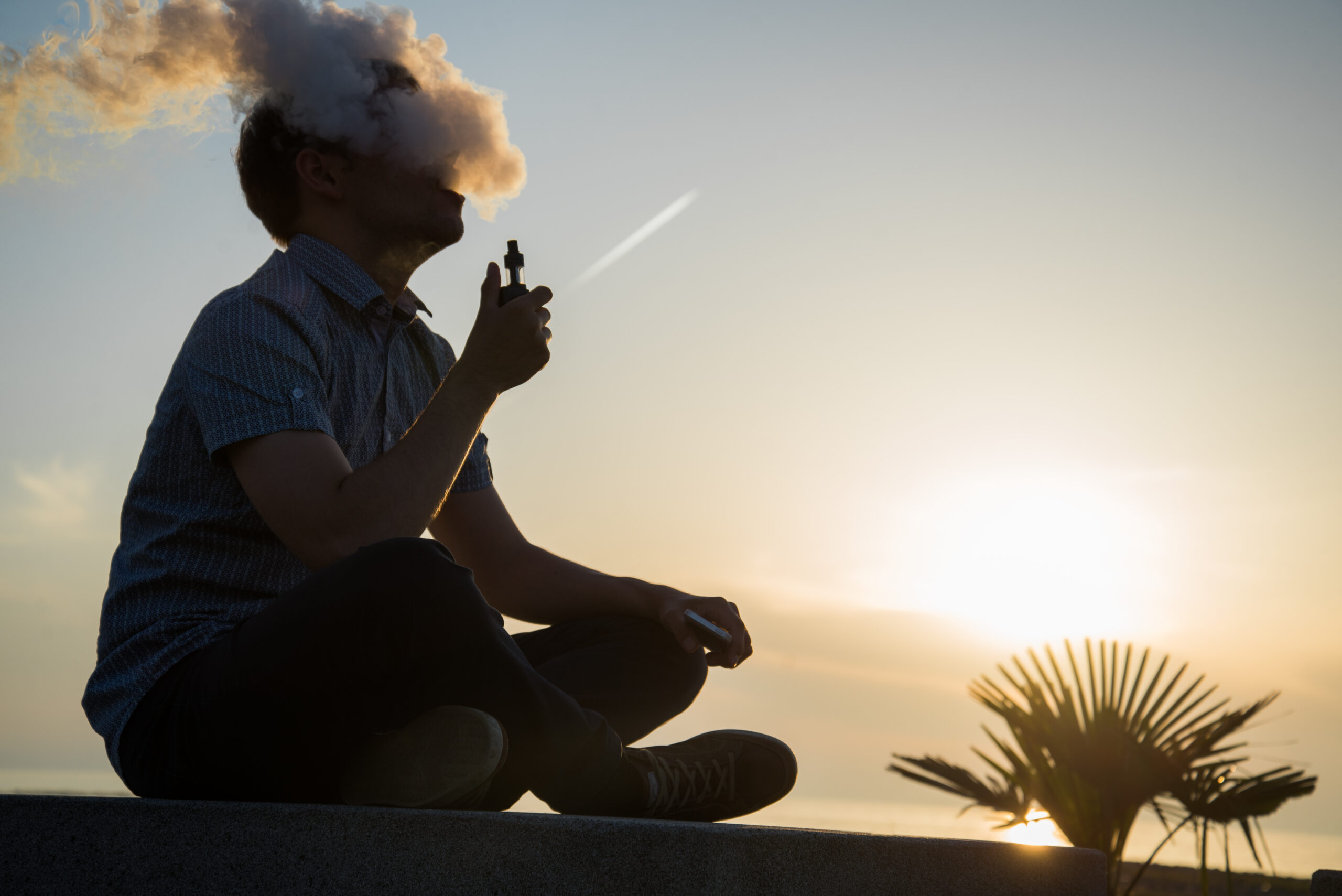 Man vaping outdoors at sunset, illustrating the risks of vaping after wisdom teeth removal